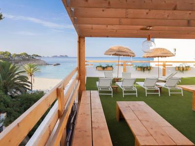 View from a covered terrace onto a beach with sun loungers and umbrellas.