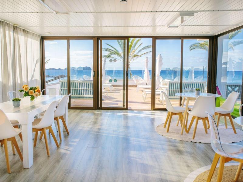 Bright, modern dining room with large windows, wooden floor, and view of terrace and sea.