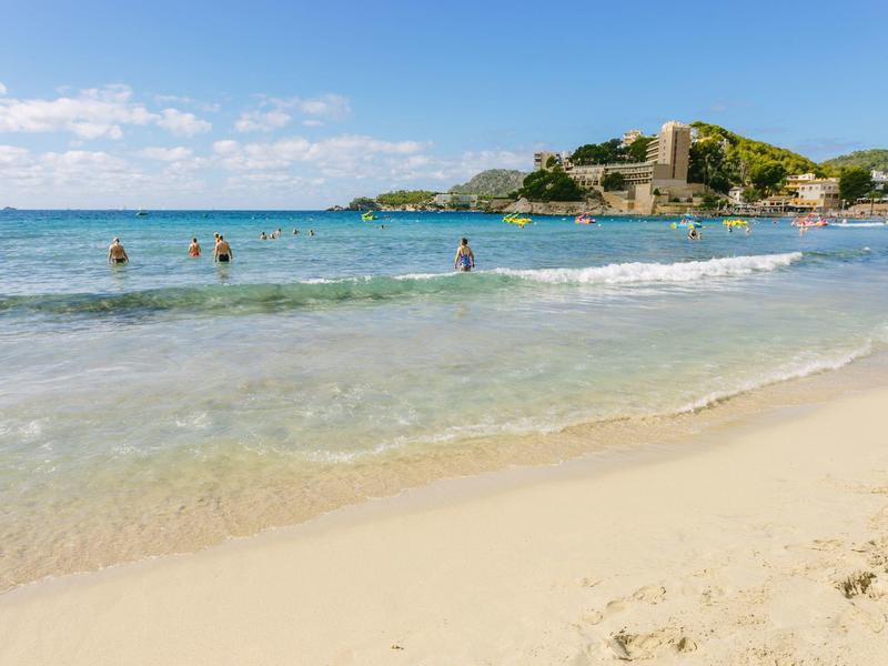 Beach with clear water, some swimmers, and a castle in the background under a blue sky