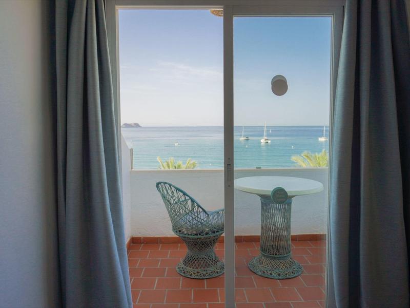 View from a hotel room to a balcony with chair and table and the sea in the background.