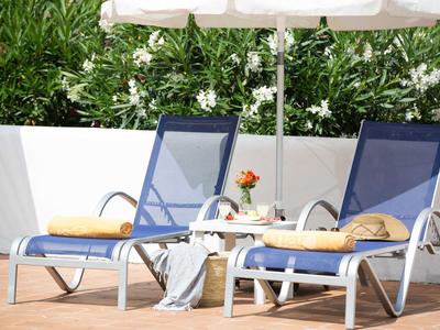 Zwei blaue Liegestühle mit gelben Handtüchern auf Terrasse neben Tisch mit Blume und Sonnenschirm.