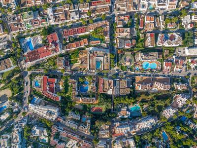 Luftaufnahme einer Stadt mit Hotels, Straßen, Pools und viel Grün rund um Urlaubsanlagen.