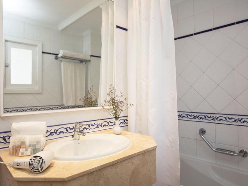 Bright hotel bathroom with tiled walls, a large mirror, sink, and a shower with white curtain.