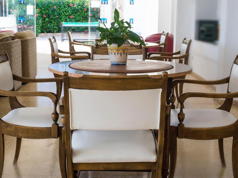 Wooden dining table with white cushioned chairs in a bright, modern living area.