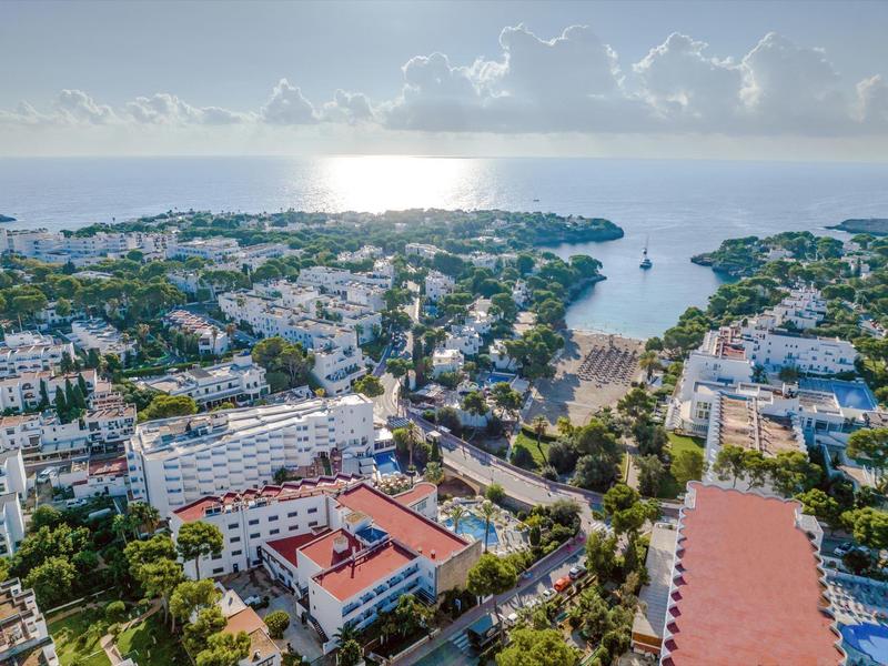 Aerial view of a coastal town with hotels, beach, and calm sea at sunset.