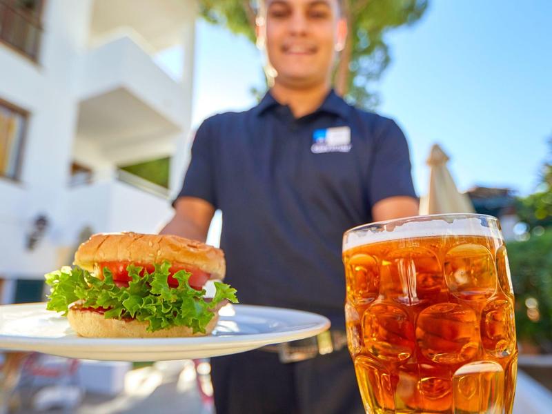 Waiter serving a burger and glass of iced tea outdoors on a sunny day.