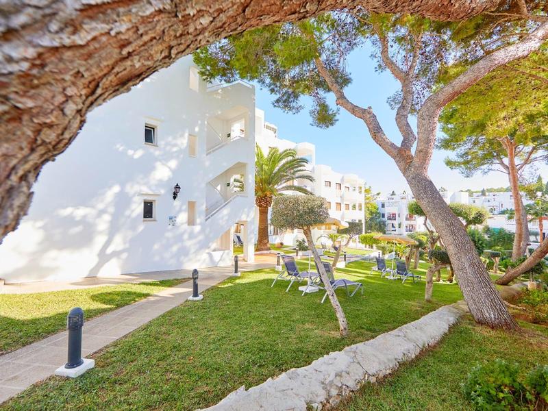 White buildings surrounded by green trees and manicured lawns in a hotel area.