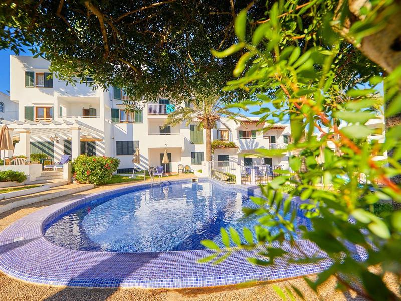 Round pool with blue tiles in front of modern multi-story apartments on a sunny day.