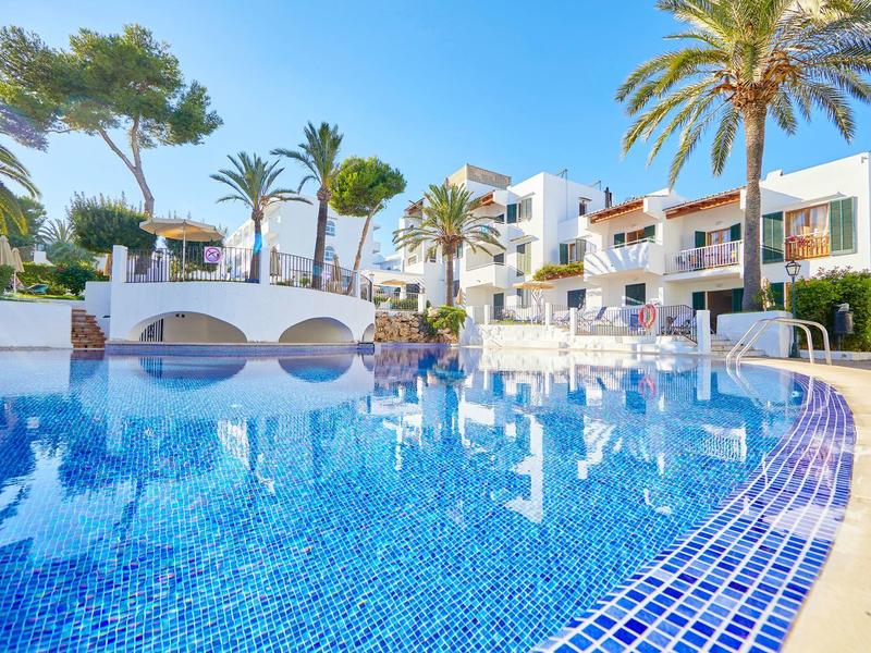 Modern hotel pool with mosaic tiles, surrounded by palm trees and white buildings.