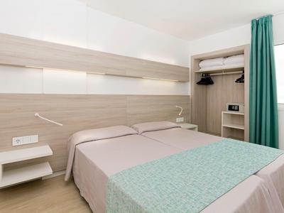 Habitación de hotel sencilla con cama doble, mesas auxiliares y cortina verde en una ventana.