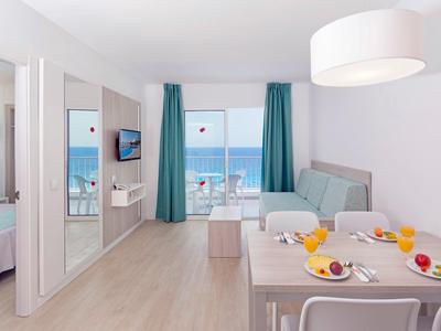 Habitación de hotel luminosa con vista al mar, mesa de comedor y asientos cómodos junto a la ventana.