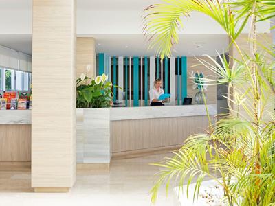 Accogliente hall dell'hotel luminosa con reception, piante e personale cordiale sullo sfondo.