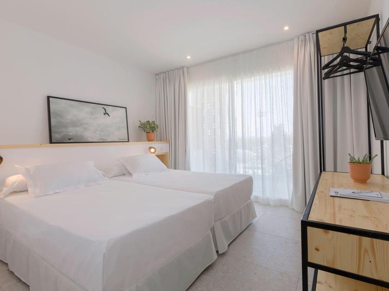 Camera d'hotel moderna con letto matrimoniale, grande finestra e arredamento minimalista.