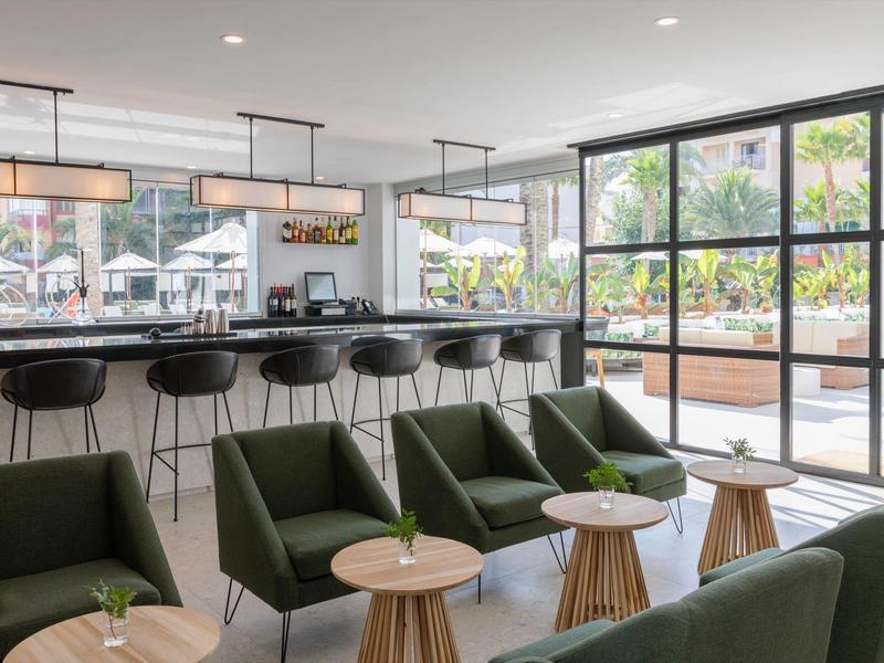 Bar dell'hotel moderno con sgabelli neri e poltrone verdi vicino a grandi finestre.