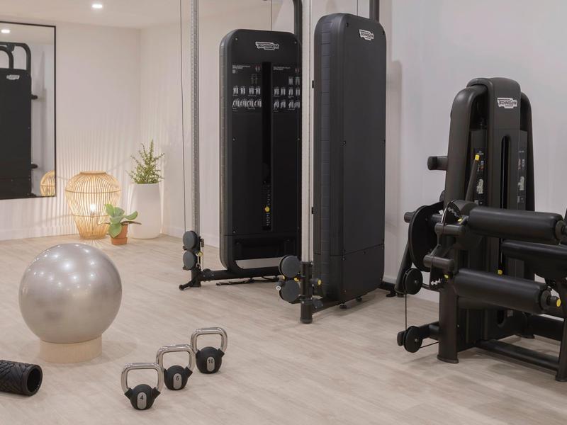 Palestra moderna con macchine per la forza, kettlebell, manubri e palla da ginnastica argento in una stanza luminosa.