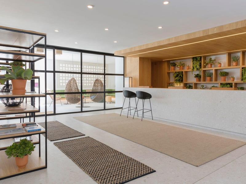 Hall di un hotel moderno con arredamento minimalista, piante e un bancone alto.