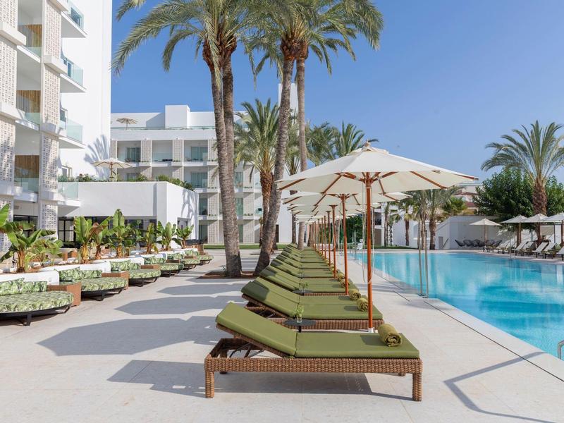 Area piscina dell'hotel con lettini e ombrelloni accanto a palme sotto un cielo limpido.
