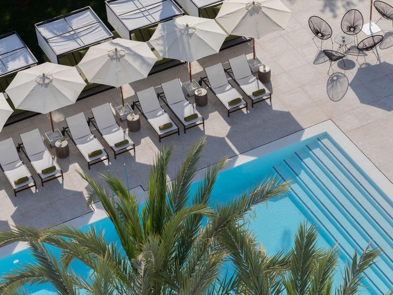 Vista di una piscina con lettini e ombrelloni accanto a palme in un hotel.