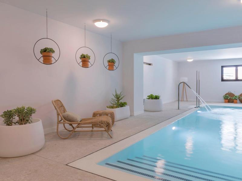 Piscina interna moderna con sedia a sdraio, piante e ambiente luminoso e pulito.