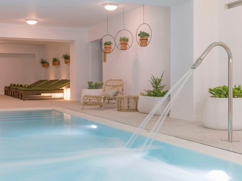 Piscina interna moderna con getti d'acqua e aree salotto accoglienti in una stanza luminosa.