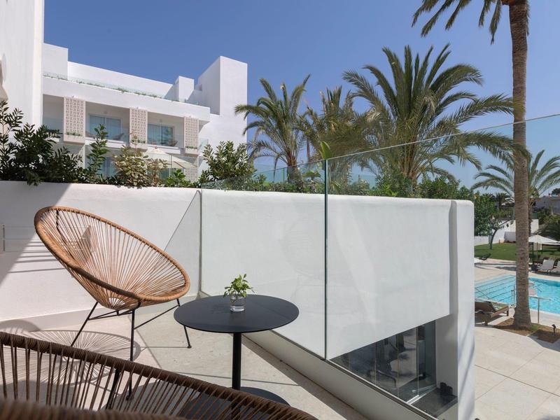 Balcone con sedie moderne e tavolo, vista su palme e piscina dell'hotel al sole.