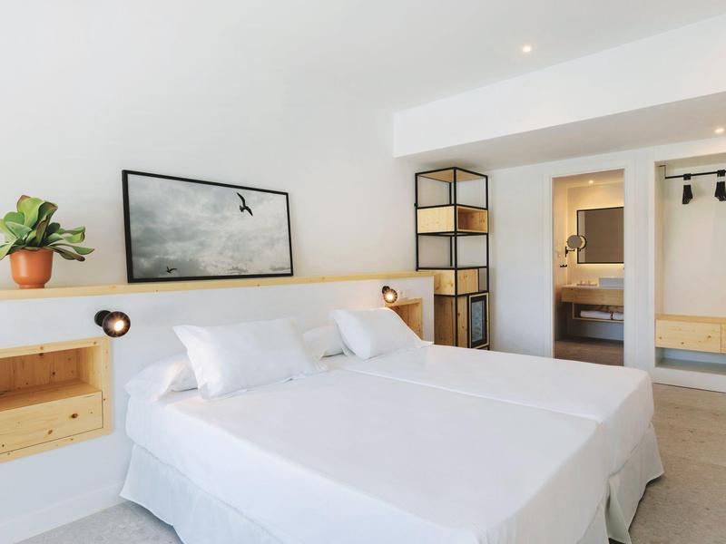 Camera doppia moderna con biancheria bianca, scaffalature incorporate e bagno adiacente.