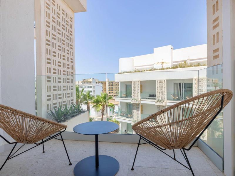 Balcone con due sedie e piccolo tavolo con vista su moderni edifici dell'hotel sotto cielo sereno.