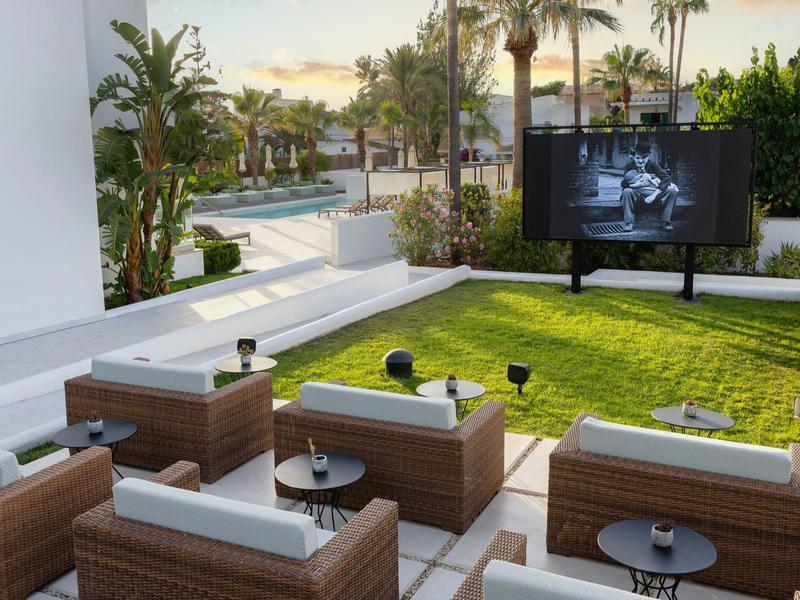 Area esterna moderna con posti a sedere e grande schermo davanti a una piscina al tramonto.