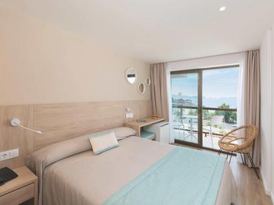 Habitación de hotel moderna con cama doble, escritorio y balcón con vista al mar.