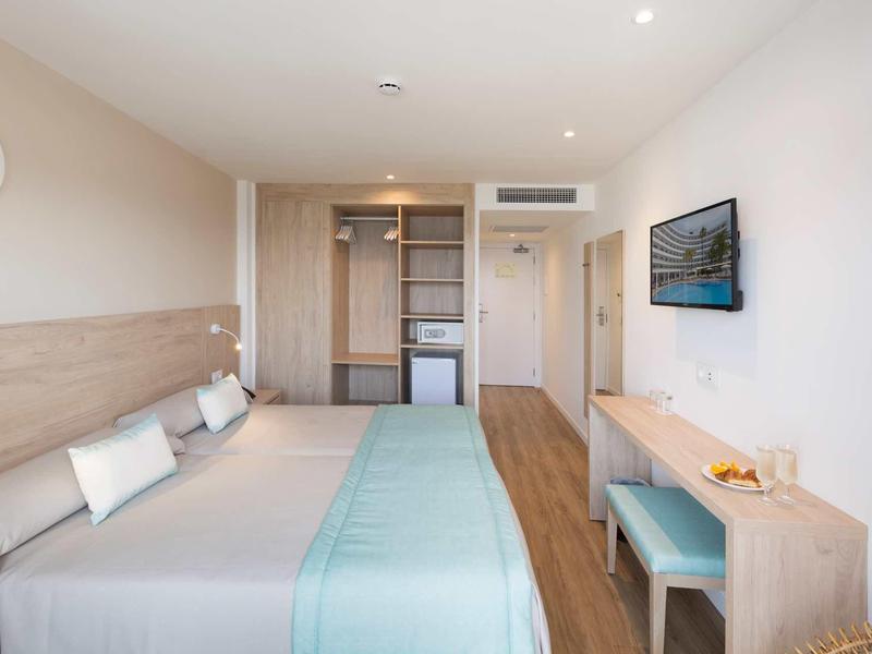 Habitación de hotel moderna con cama doble, televisor de pared y suelo de madera clara.