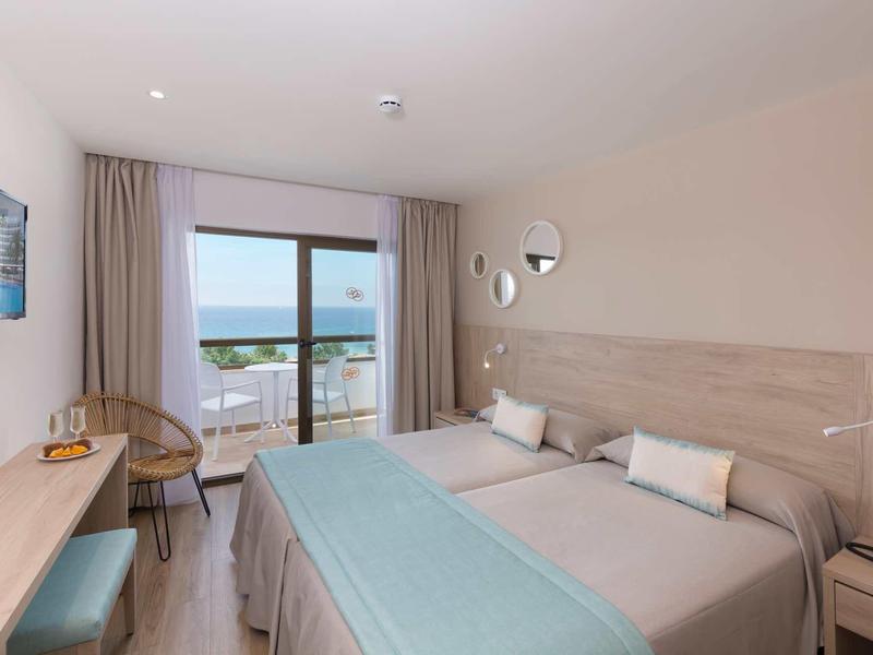 Habitación de hotel moderna con cama doble, vista al mar y muebles de madera clara.
