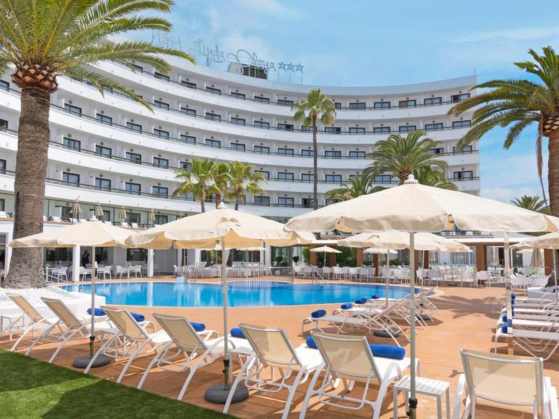 Un hotel con edificio curvo, piscina, sombrillas y tumbonas bajo palmeras.