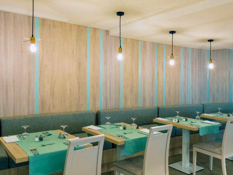 Restaurante moderno con paredes de madera, caminos de mesa verdes y sillas blancas en un hotel.