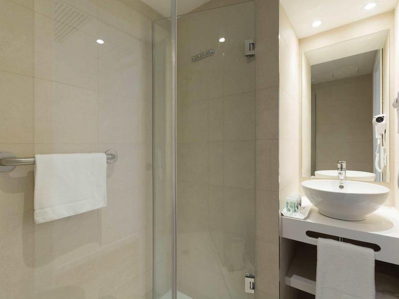 Baño moderno de hotel con ducha de vidrio, lavabo redondo y toallas.