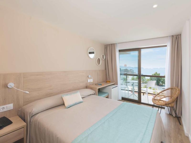 Habitación de hotel moderna con cama doble, escritorio y balcón con vista al mar.