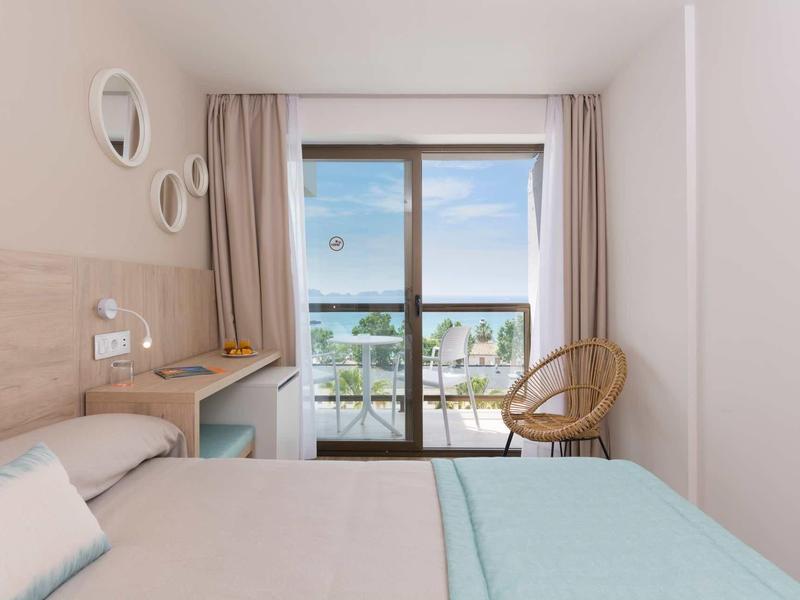 Habitación de hotel luminosa con cama doble, balcón con vistas y decoración en tonos beige y azul