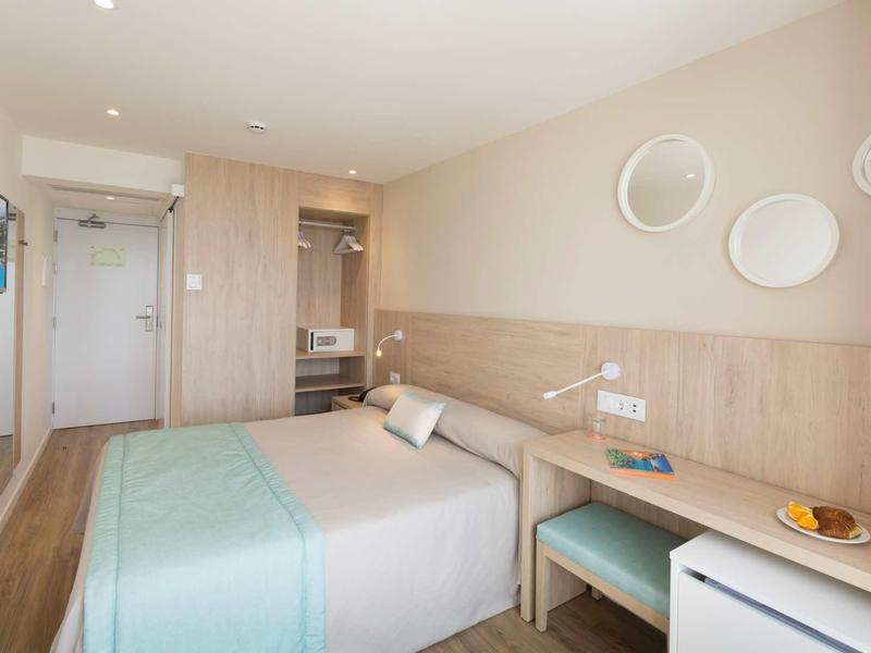 Habitación de hotel luminosa con cama doble, televisor, escritorio y decoración minimalista.