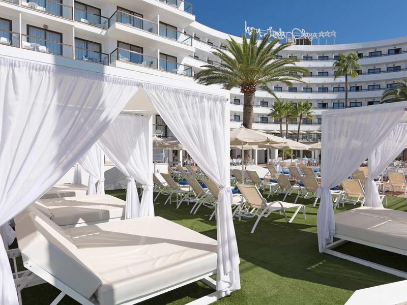 Terraza moderna de hotel con camas con dosel blancas y palmeras bajo cielo azul.