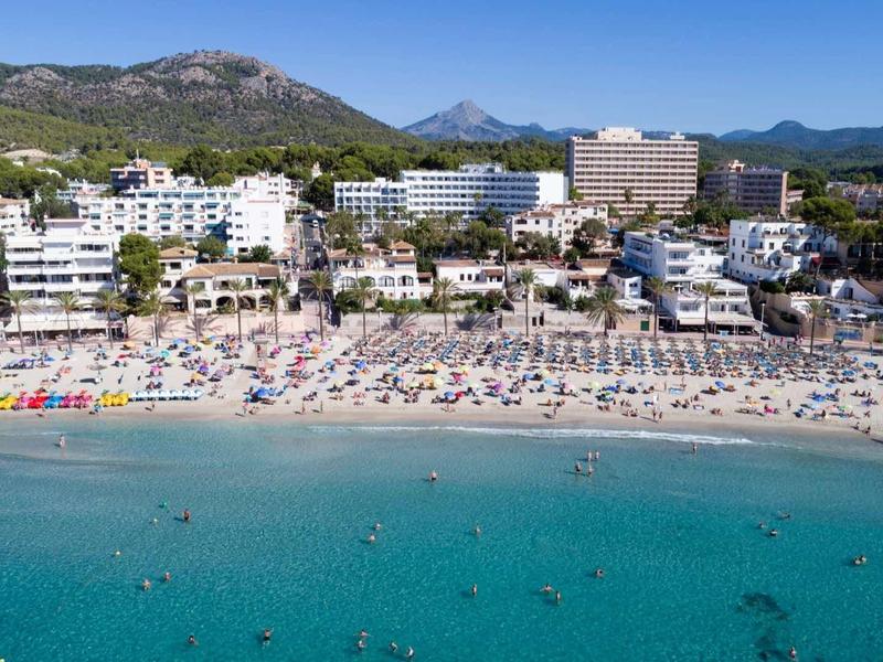 Amplia playa de arena con tumbonas y hoteles con montañas al fondo junto al mar.