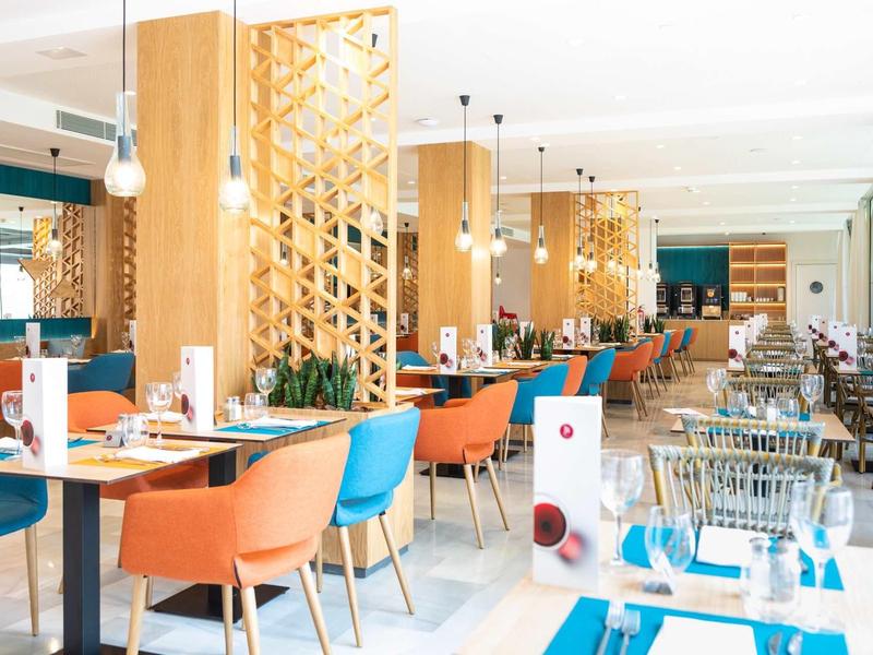 Helles Restaurant mit bunten Stühlen, Holzsäulen und modernem, freundlichem Ambiente.