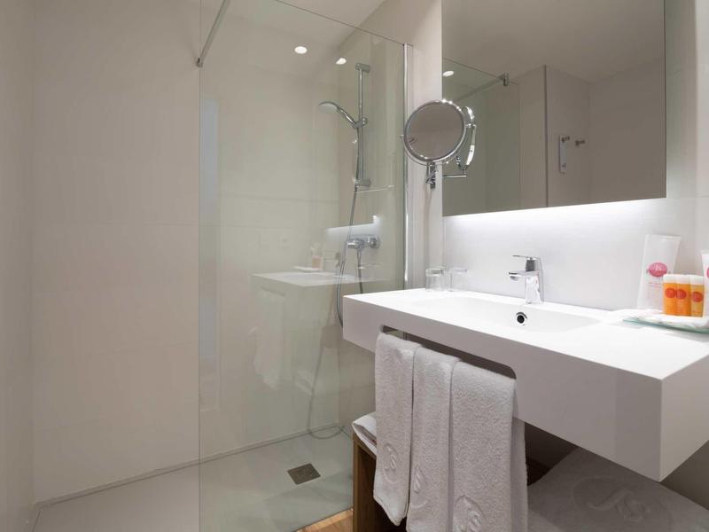 Modernes, weißes Badezimmer mit Glasdusche, großem Spiegel und samtweißer Waschtischfläche.