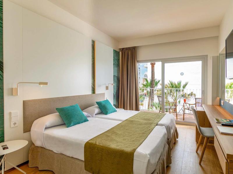 Helles Doppelzimmer mit Holzfußboden, zwei Betten, grünen Akzenten und Terrasse mit Pflanzen.