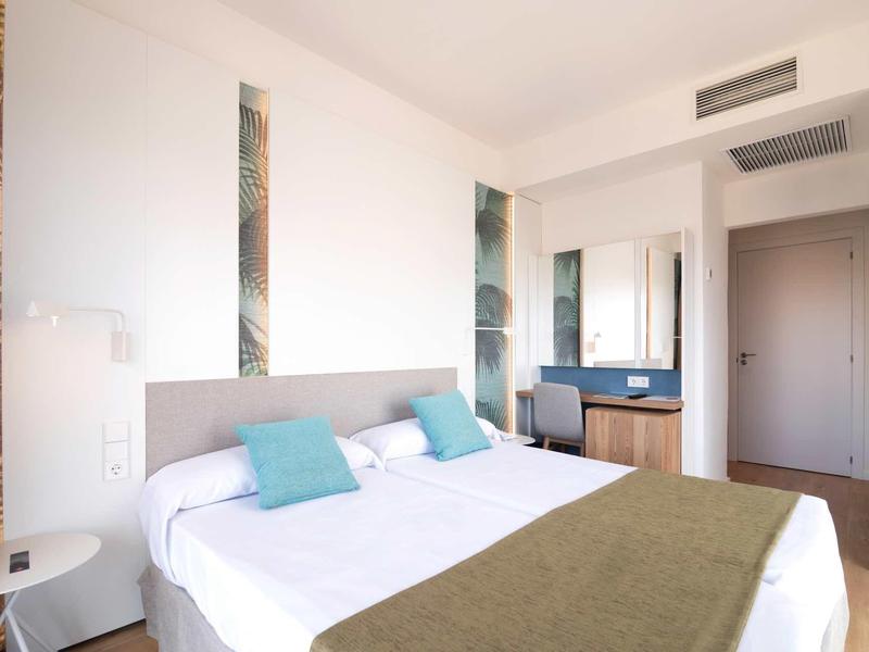 Helles modernes Schlafzimmer mit großem Bett, weißen Wänden, grünen Akzenten und Holzkommode.