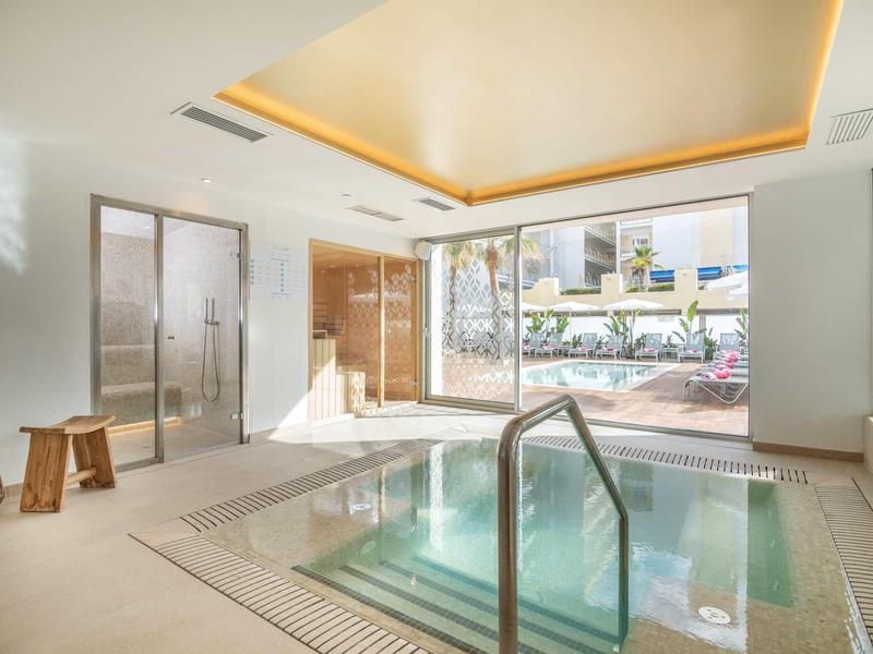 Helle Spa-Landschaft mit quadratischem Whirlpool, Glaswand und warmem Deckeneinbau.