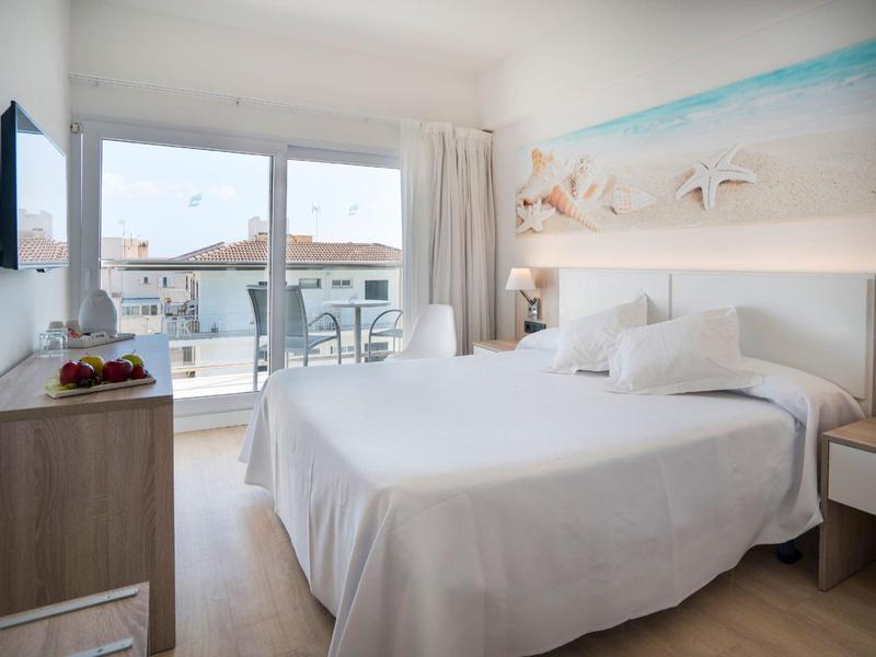 Helles Hotelzimmer mit Doppelbett, Meerblick, Balkon, weißer Einrichtung und Holzfußboden.