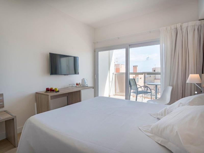 Helles Schlafzimmer mit großem Bett, TV an der Wand und Balkon mit zwei Stühlen und Tisch.