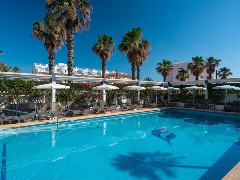 Außenpoolbereich mit Liegestühlen, Sonnenschirmen und Palmen unter klarem blauem Himmel.