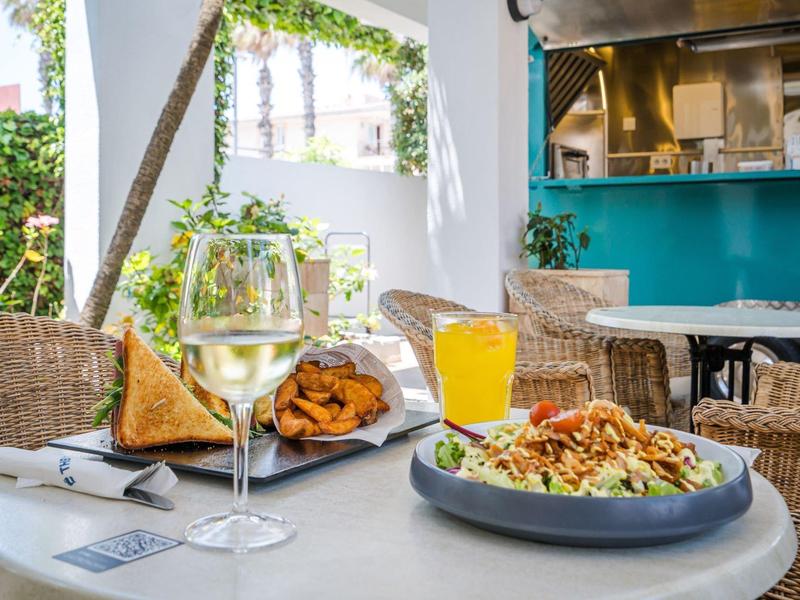 Tisch mit Glas Weißwein, Orangensaft und Tellern mit Snacks in gemütlicher Außengastronomie.