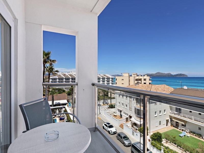 Balkon mit runder Tischplatte, Stuhl und Glasgeländer, Blick auf Meer, Straßen und Gebäude.