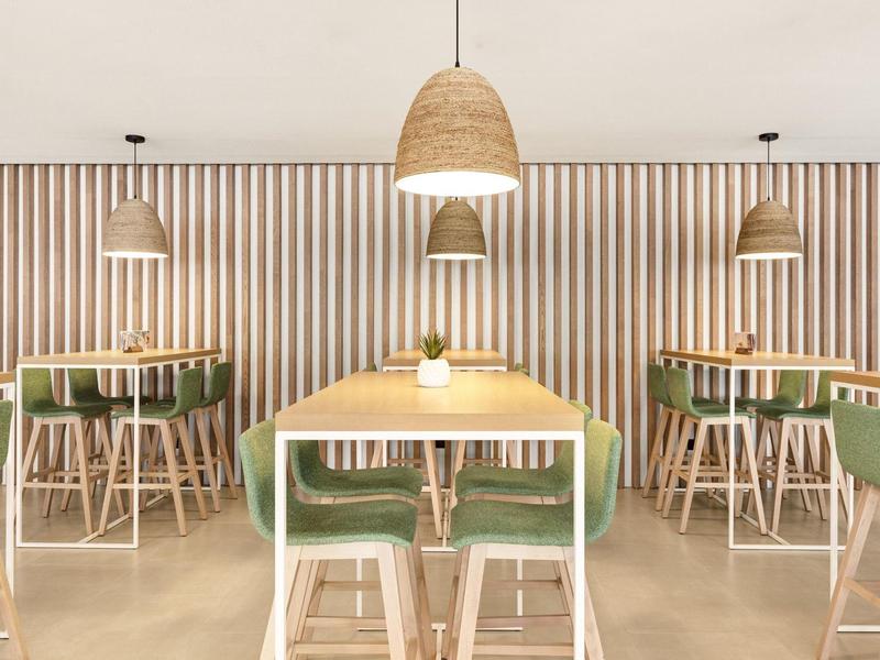Moderner Gastraum mit Holzstühlen, grünen Sitzpolstern, Lampen und gestreifter Wandgestaltung.
